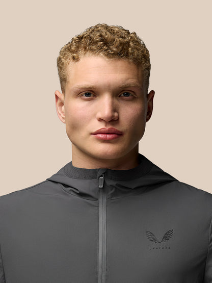 Close up of model in zipped charcoal Lightweight Flex Jacket with hood and subtle chest logo.