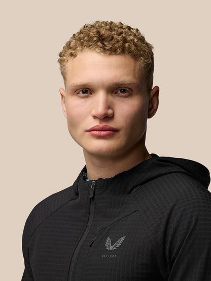 Portrait of a male model wearing a black Flex Winterised Jacket with hood, Castore logo on the chest