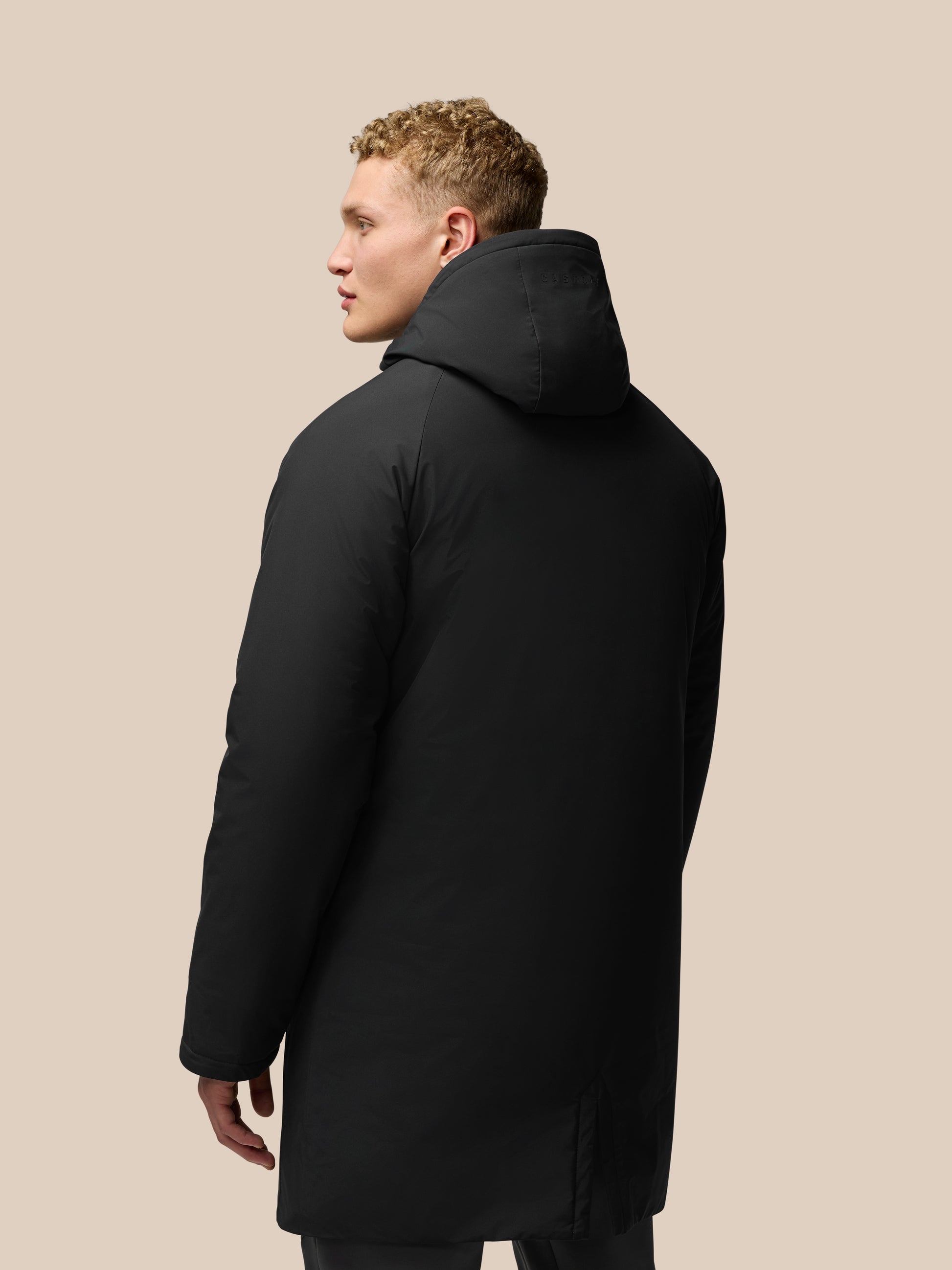 Back view of a black longline hooded jacket on a male model with the hood up
