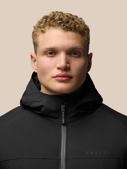 Close-up of a man wearing a black longline wadded jacket with hood and front zipper