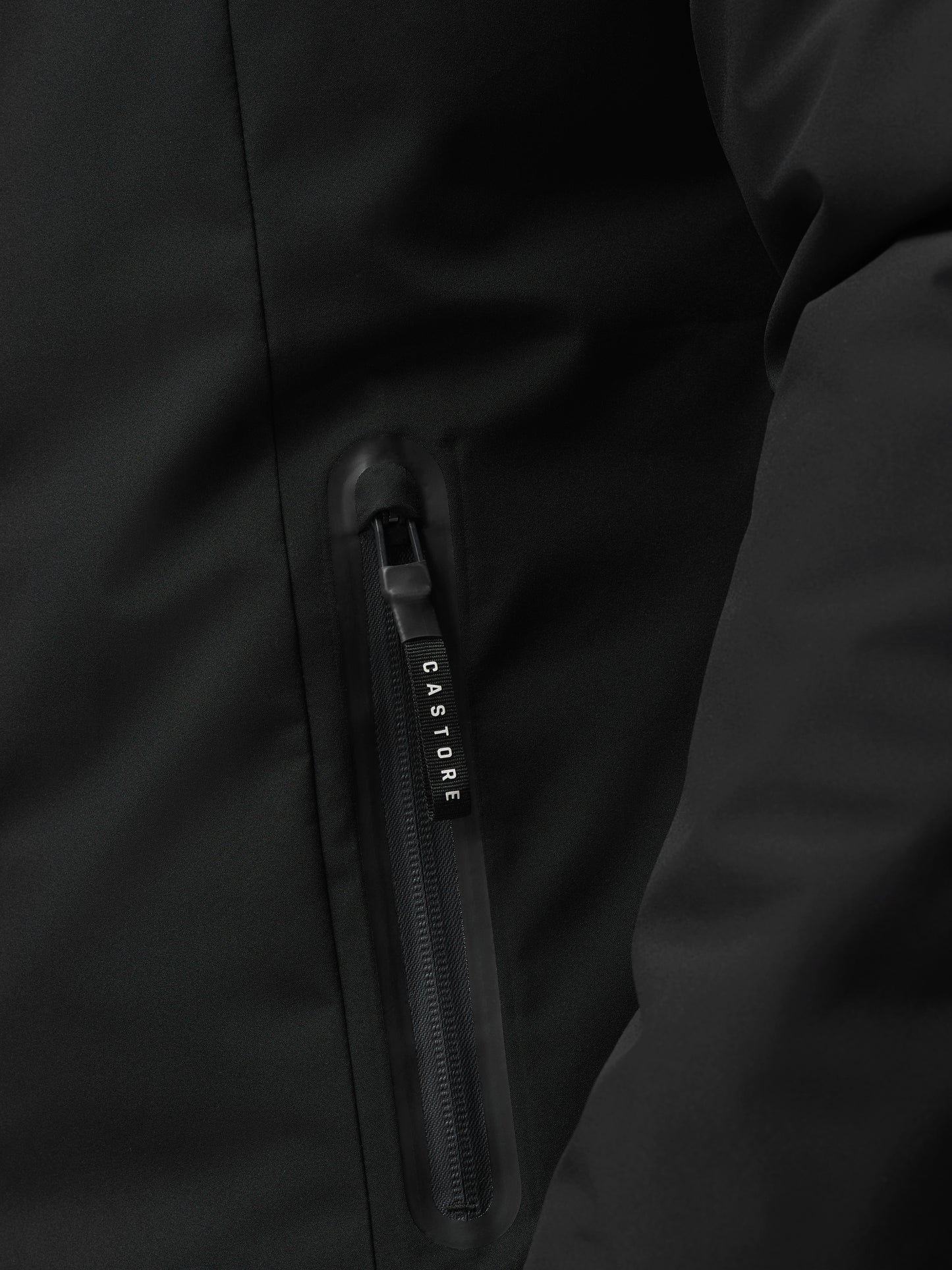 Close-up of black longline wadded jacket zipper and fabric texture with Castore branding on the pull