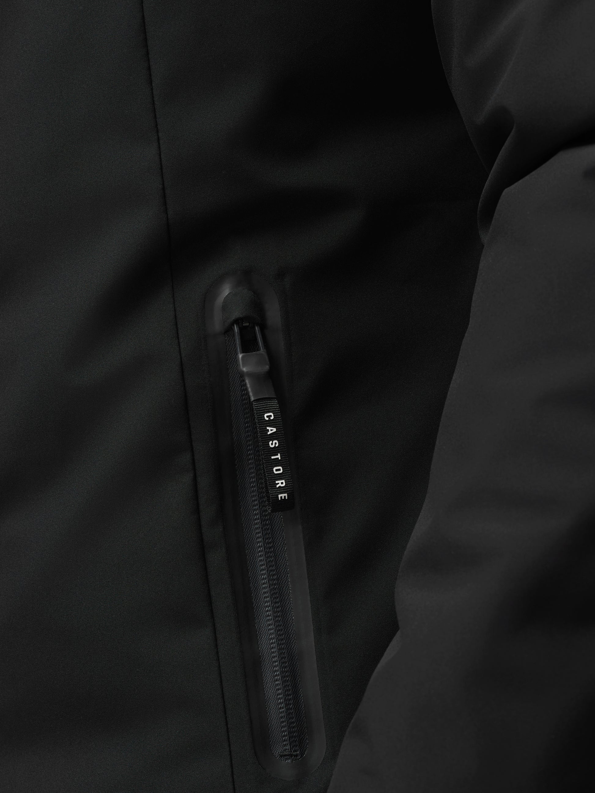 Close-up of black longline wadded jacket zipper and fabric texture with Castore branding on the pull