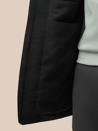 Close-up of black longline wadded jacket showing exterior pocket and subtle stitching on a beige background