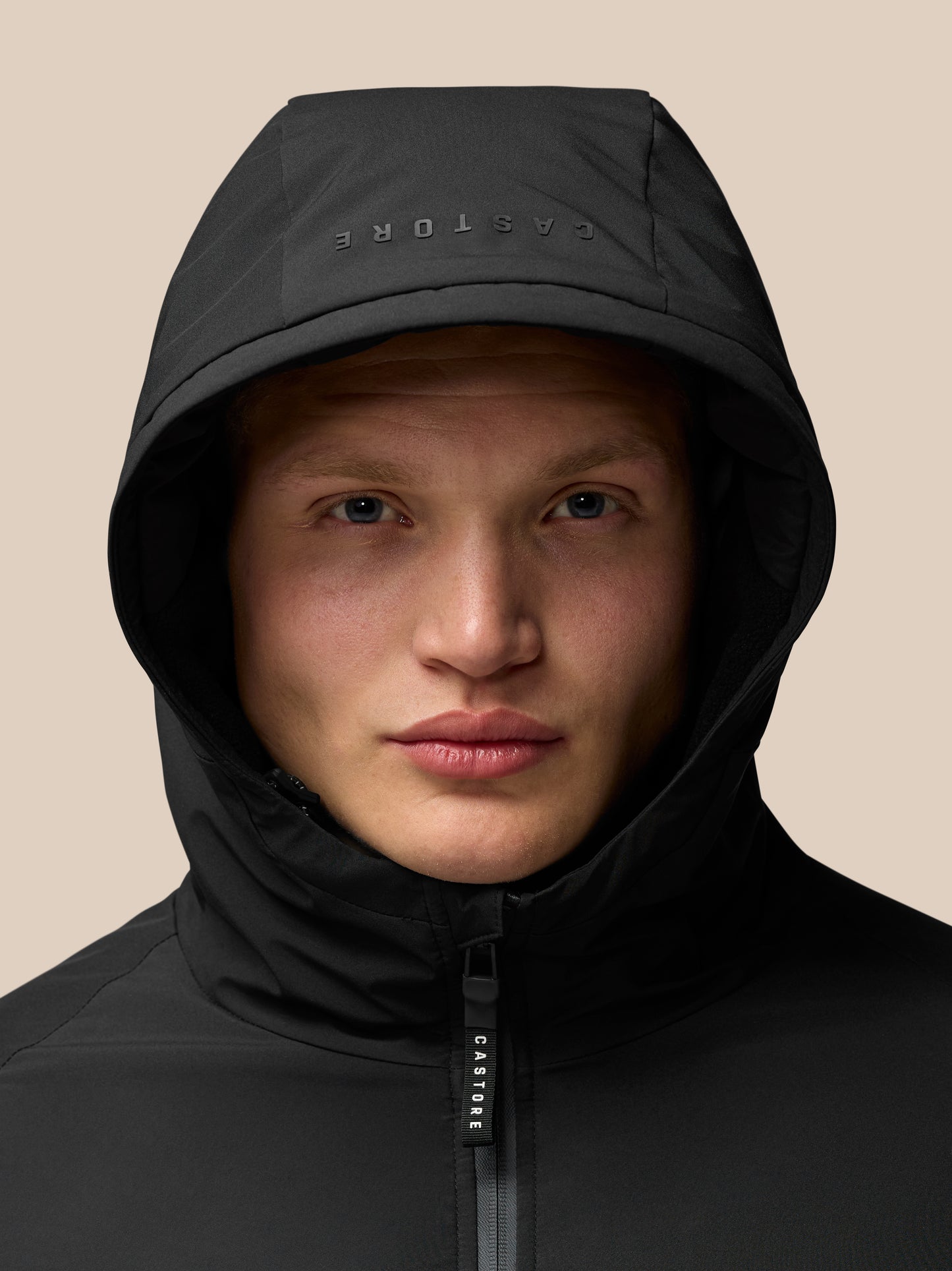Close-up of a person wearing a black hooded jacket with a center zipper and CASTORE branding on the zipper pull.