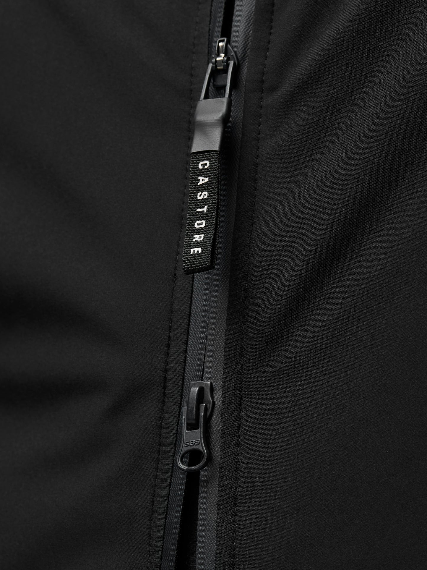Close-up of a black jacket zipper with a Castore branded pull on smooth black fabric.