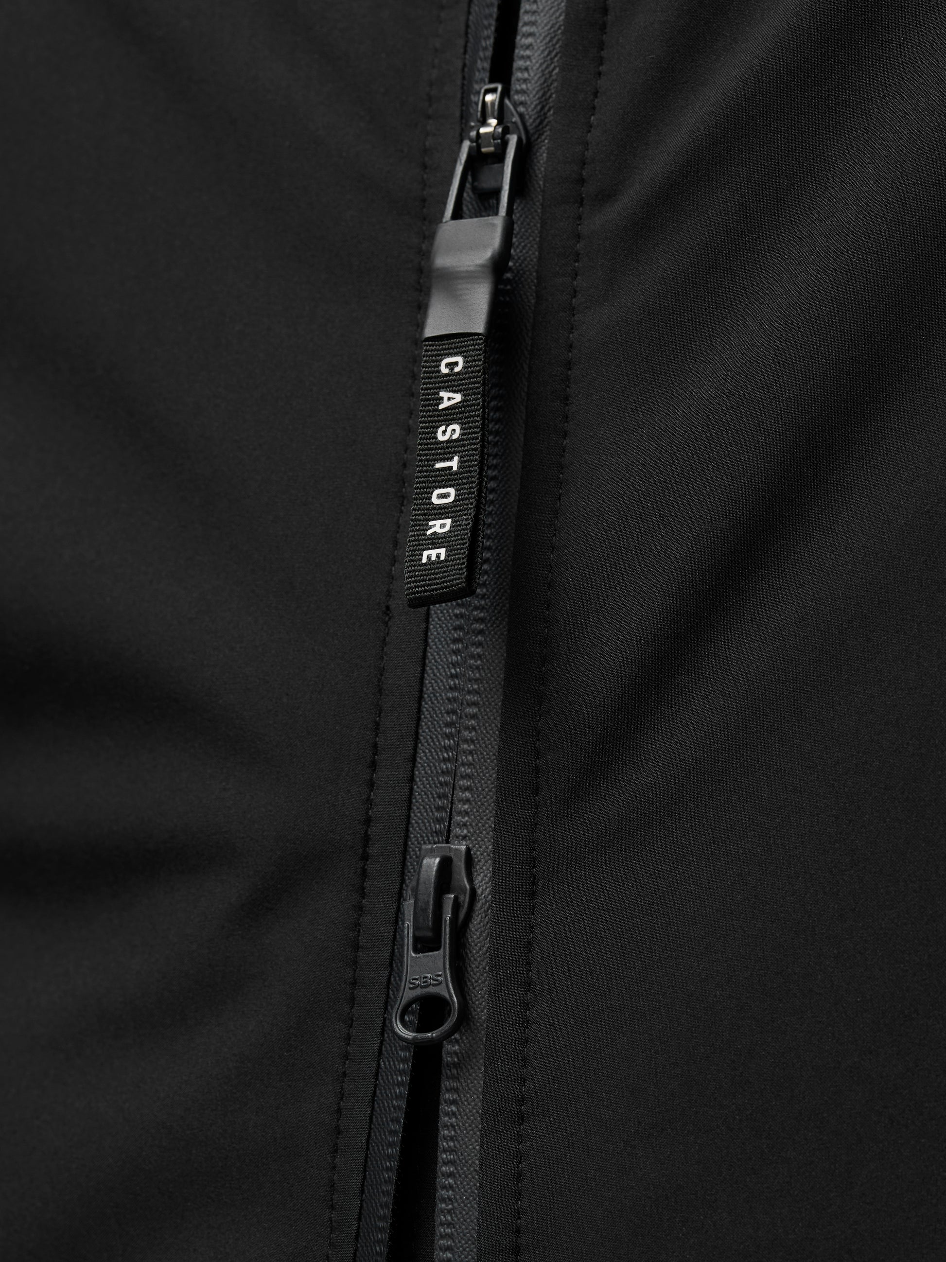 Close-up of a black jacket zipper with a Castore branded pull on smooth black fabric.