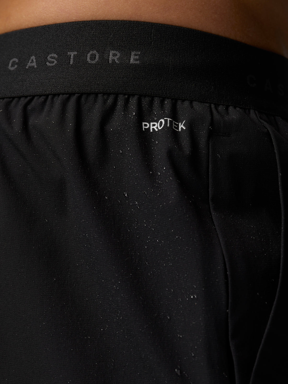 Close-up of ProTek logo on the back waistband of black Adapt Training Joggers with water droplets on fabric