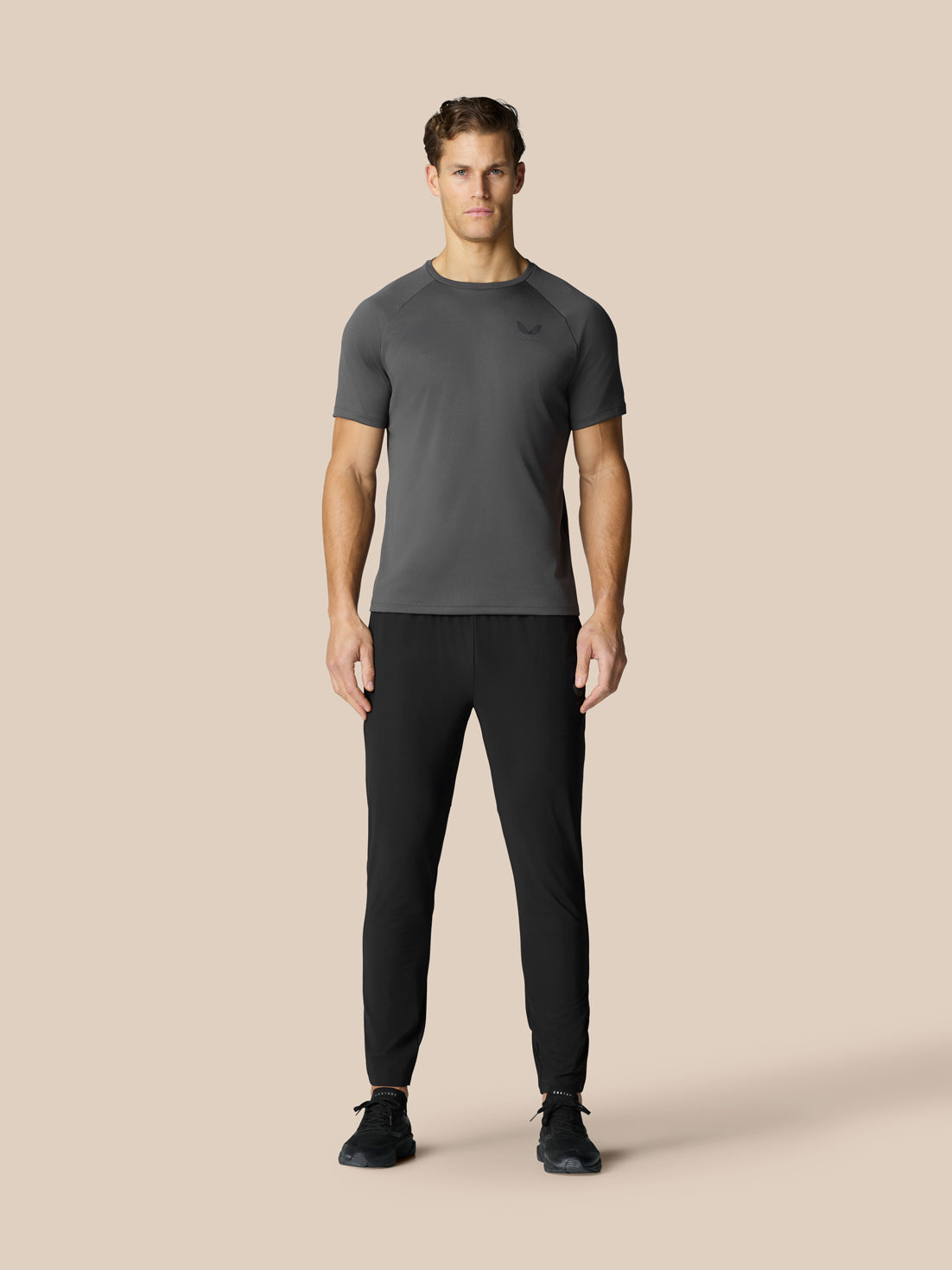 Full-body shot of a male model wearing black Adapt Tech Training Trousers with a gray athletic shirt