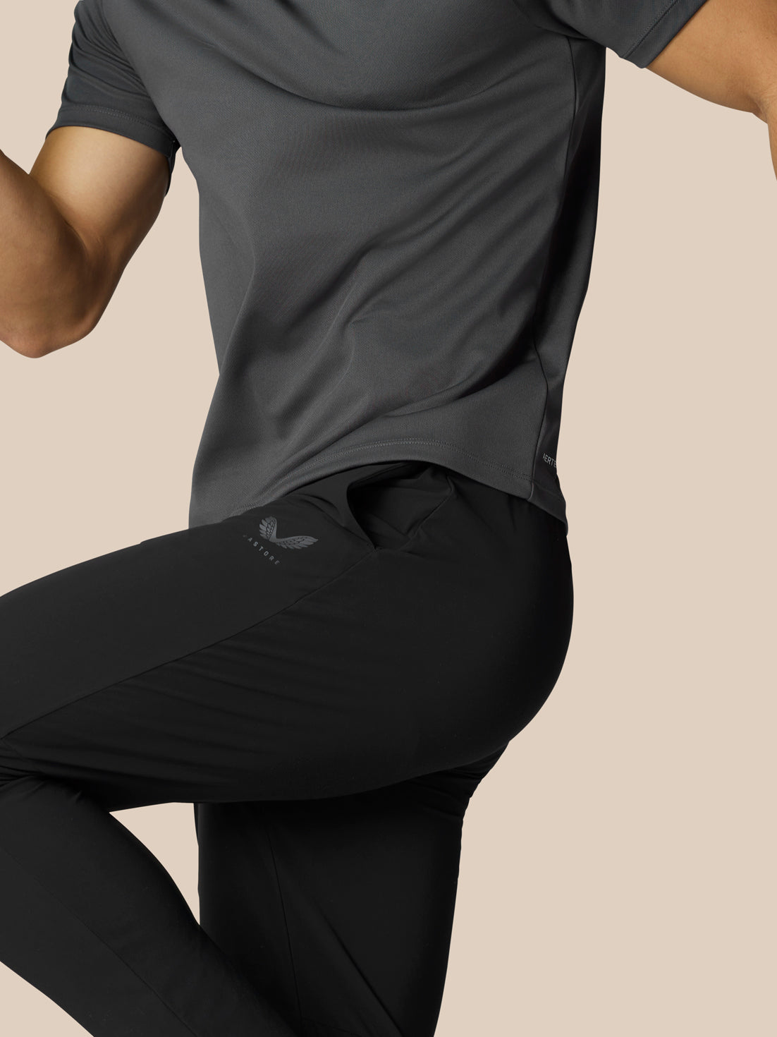 Side view of a male athlete wearing black Adapt Tech Training Trousers with a thigh logo and a gray shirt