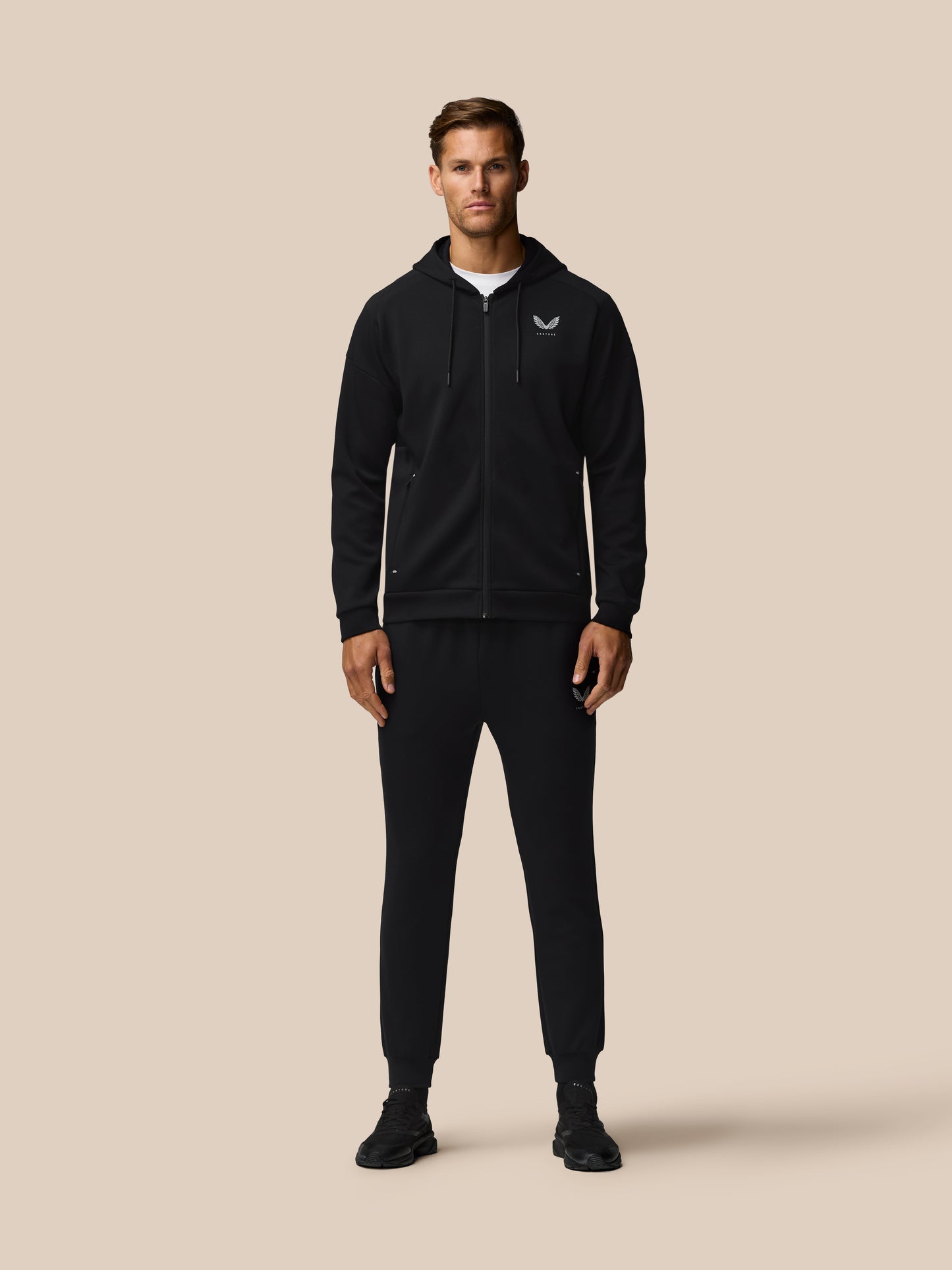 Male model in black zip hoodie with logo and matching joggers from the Travel Lifestyle collection.