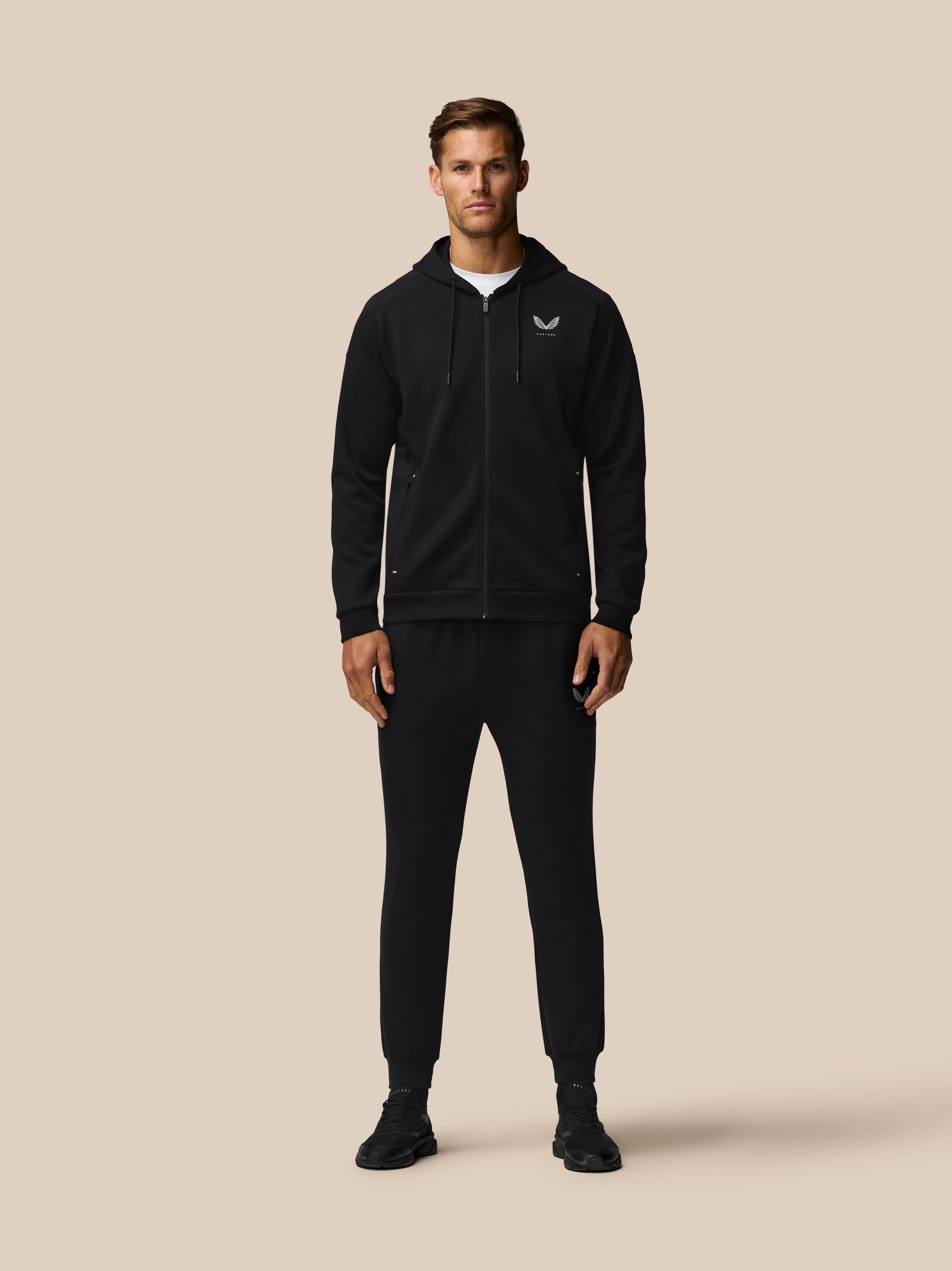 Male model in black zip hoodie with logo and matching joggers from the Travel Lifestyle collection.