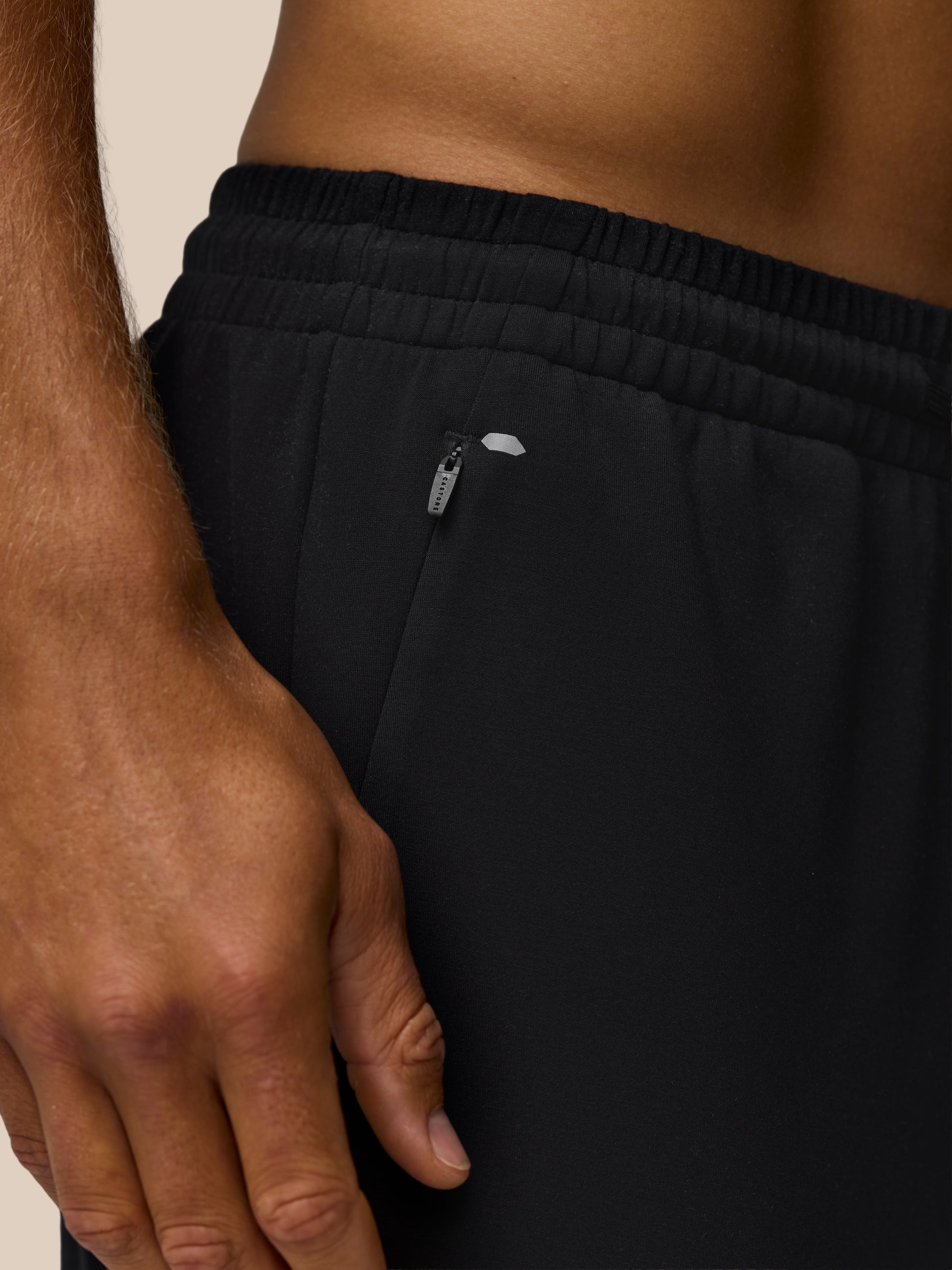 Close up of black travel joggers waistband showing elastic band and hip zip pocket.
