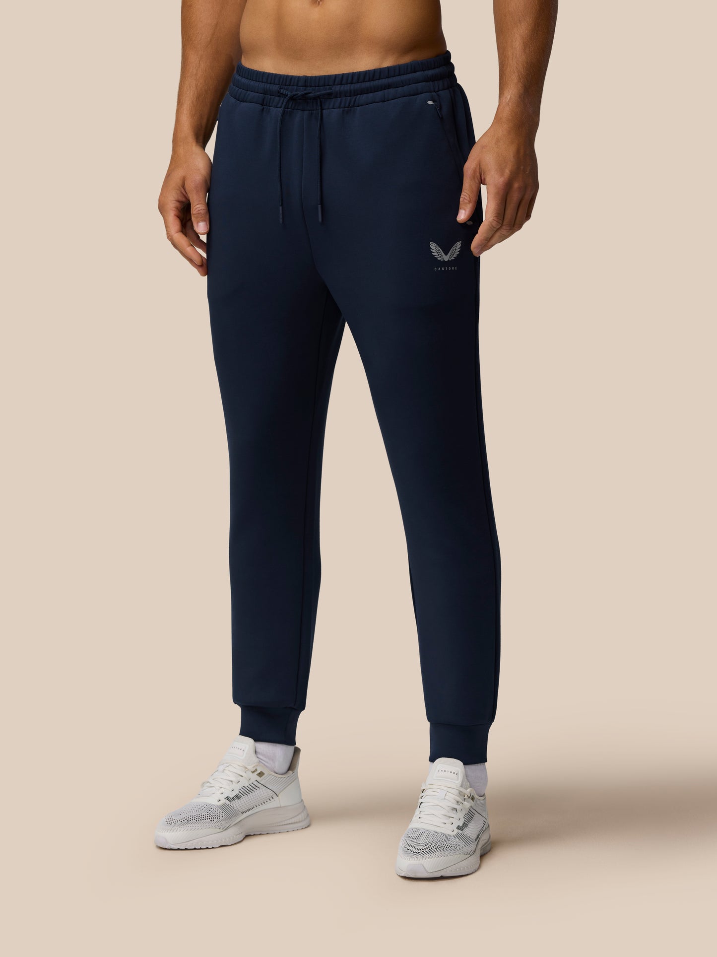 Model wearing navy Travel Lifestyle Joggers with elastic drawstring waist, tapered cuffs and Castore logo on the thigh, paired with white sneakers
