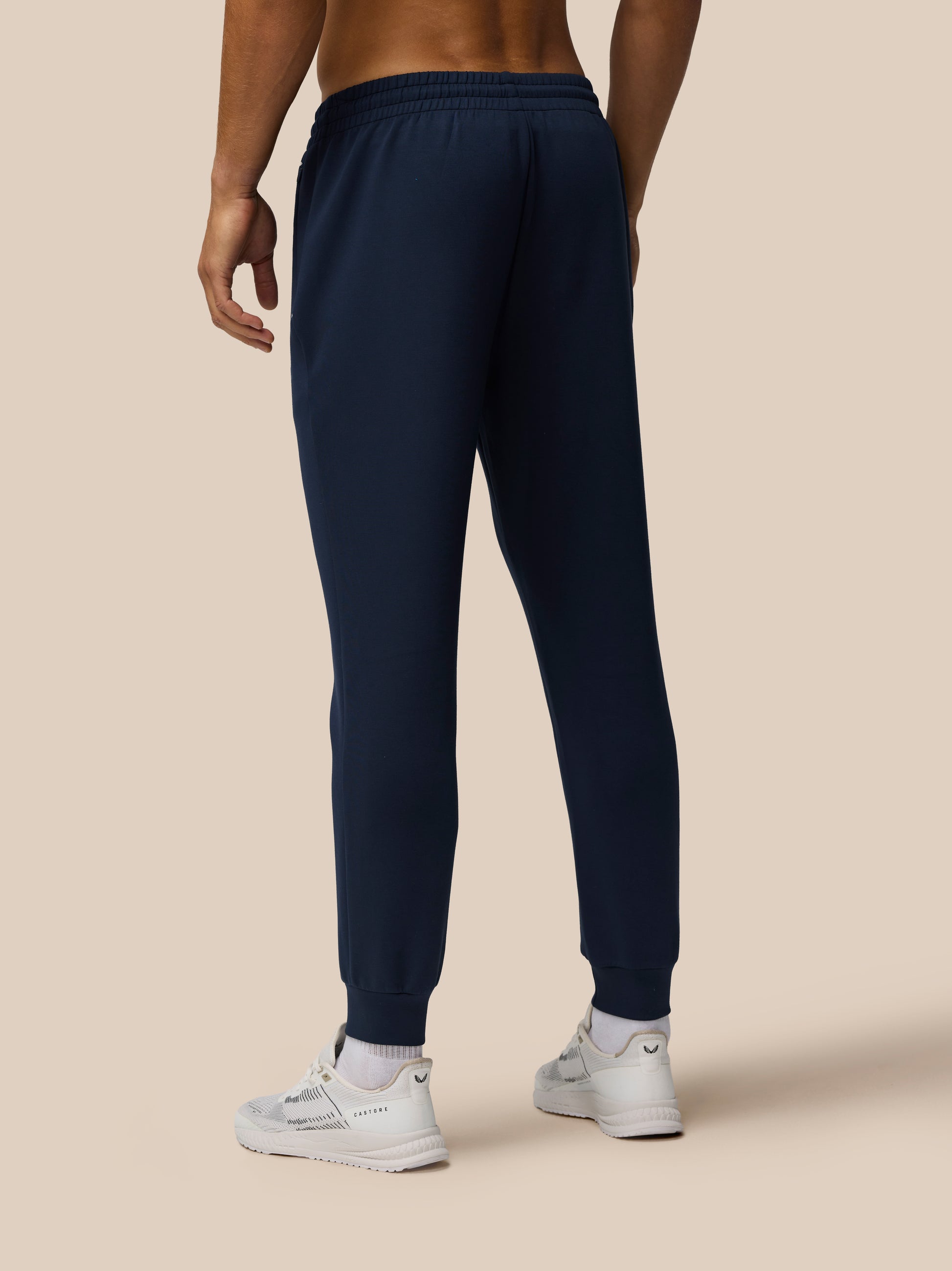 Back view of a model wearing navy Travel Lifestyle Joggers with an elastic waistband cuffed hem and Castore logo on the leg.