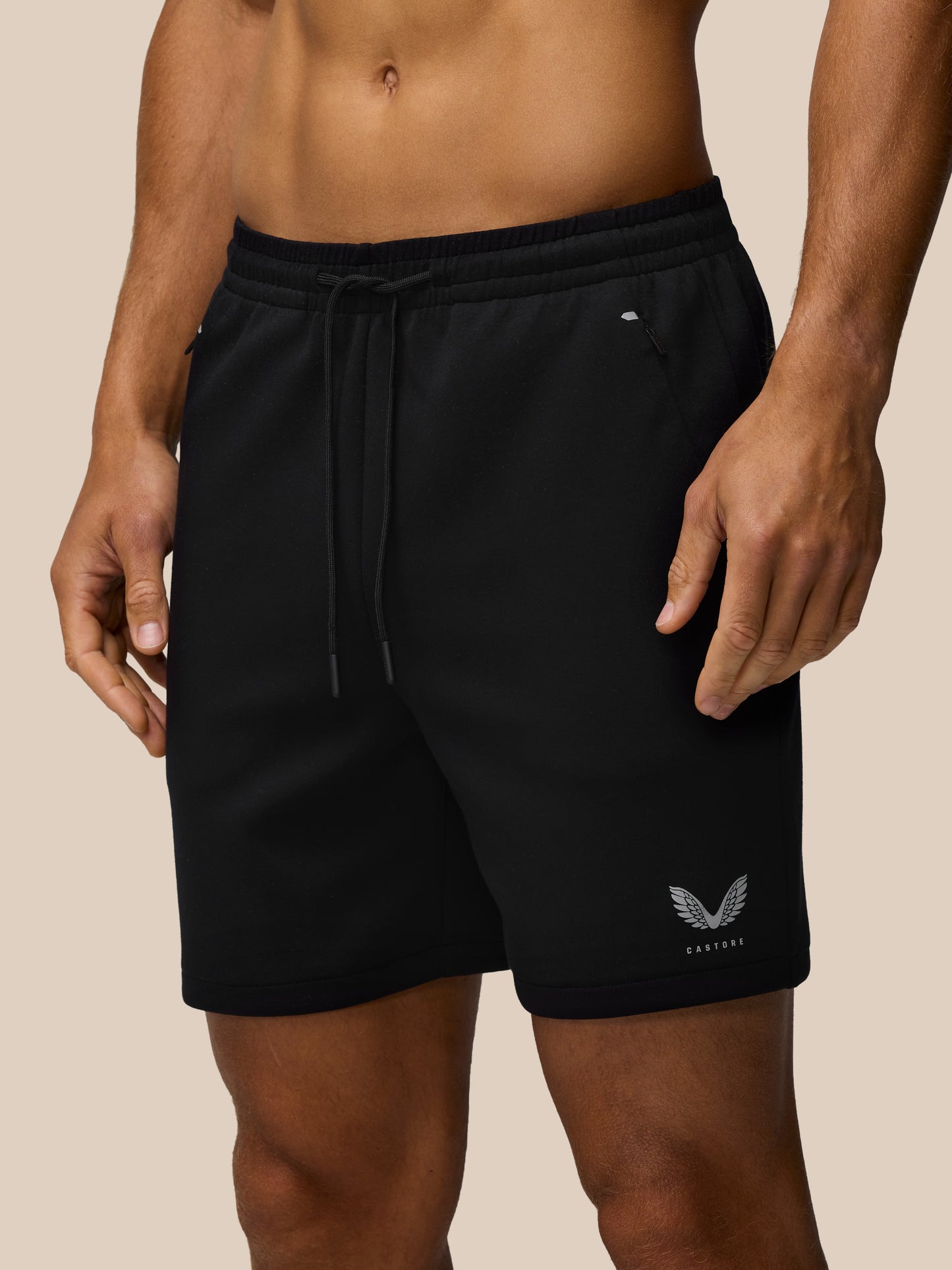 Close up of black travel shorts with elastic waistband, drawcord, concealed zip pocket, and Castore emblem at the hem.