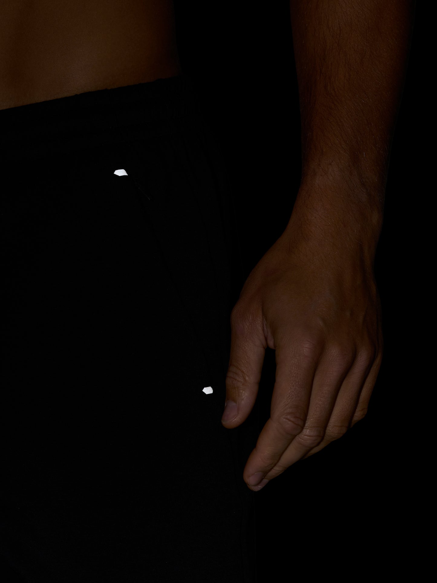 Close-up of black Travel Lifestyle Shorts fabric showing a small white logo near the hip with a hand resting beside.
