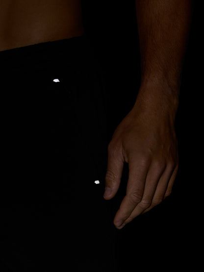 Close-up of black Travel Lifestyle Shorts fabric showing a small white logo near the hip with a hand resting beside.