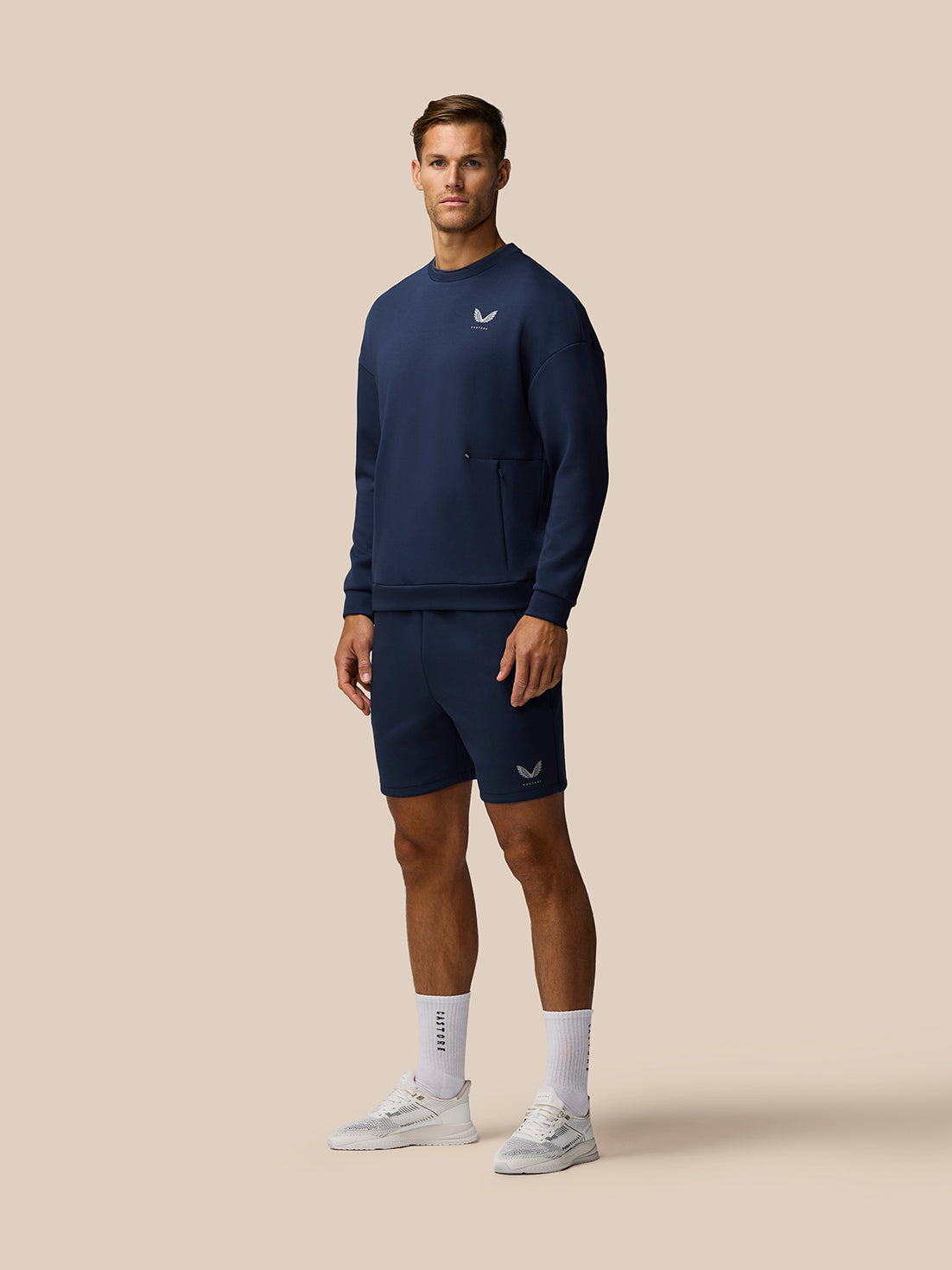 Male model in navy Travel Lifestyle Shorts with matching top and white sneakers.