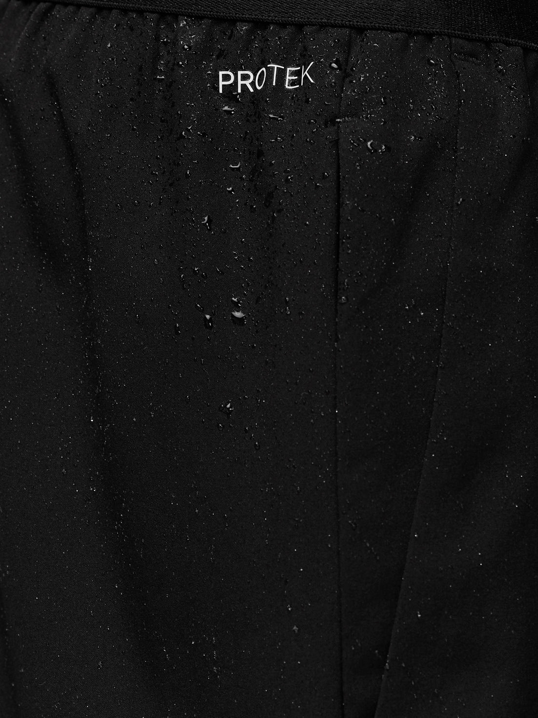 Close-up of black Adapt Training Shorts fabric with water droplets and PROTEK branding on the waistband