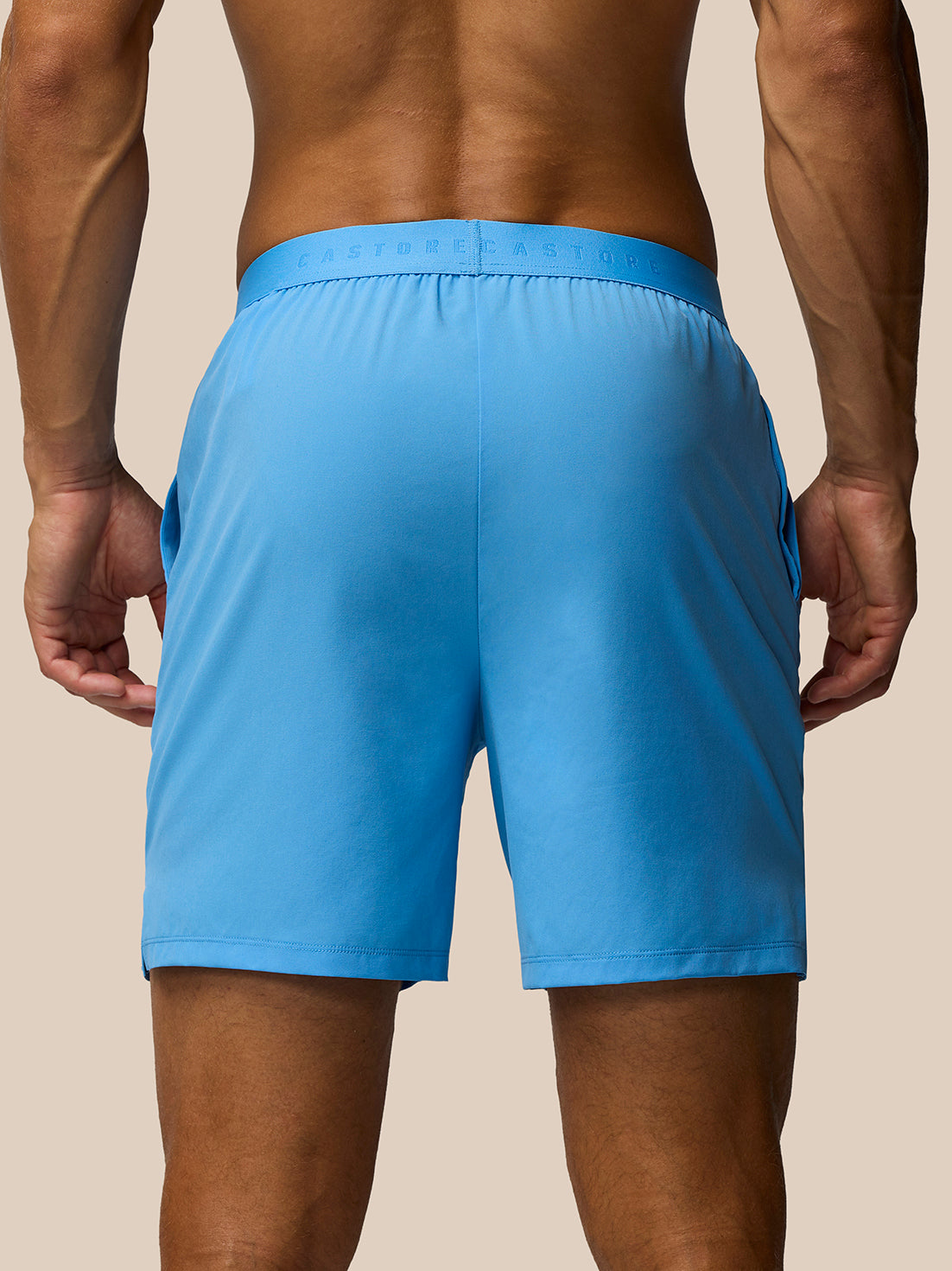 Back view of a man wearing bright blue Adapt Training Shorts showing the elastic waistband with Castore branding