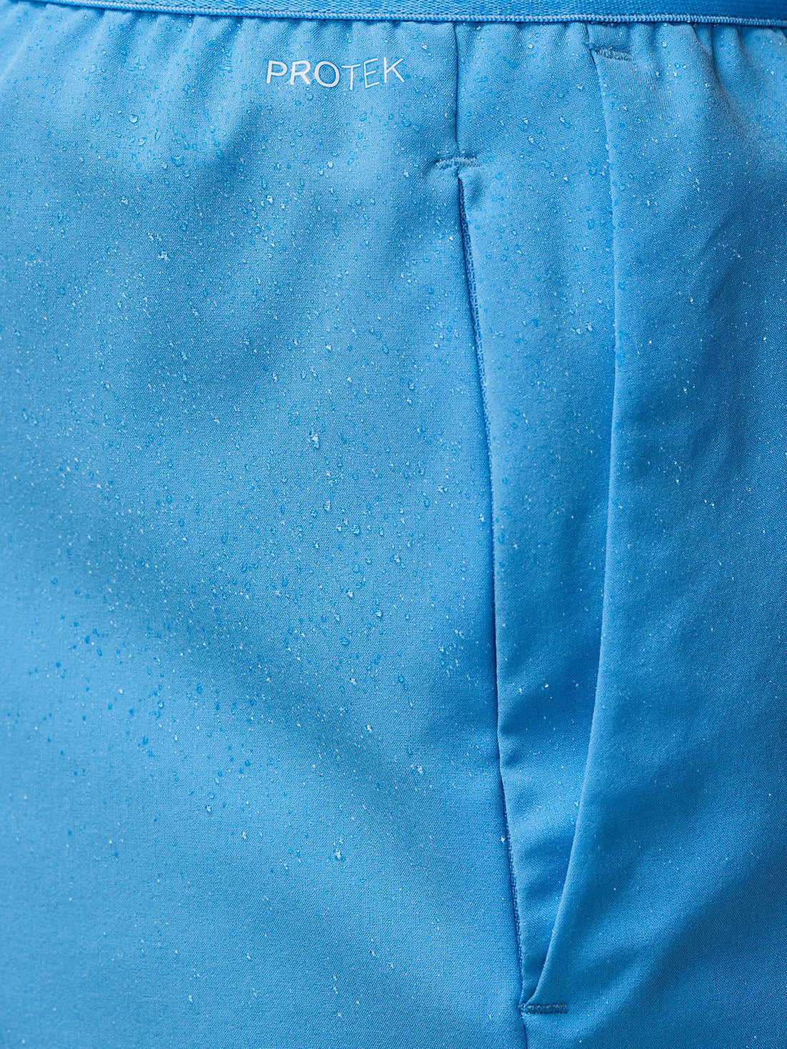 Blue waistband close up on Adapt Shorts showing ProTek branding and moisture droplets.