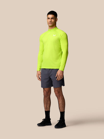 Male model wearing a neon lime long sleeve training top and gunmetal shorts against a beige backdrop.