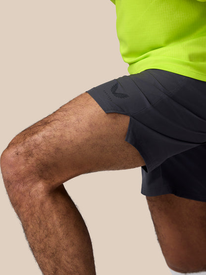 Side view of a man wearing dark Adapt Training Shorts with a Castore logo on the hem and a neon green top.