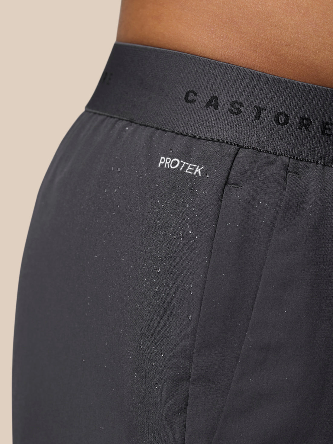 Close-up of the waistband area on gunmetal Adapt Training Shorts showing Castore branding and PROTEK moisture on fabric.