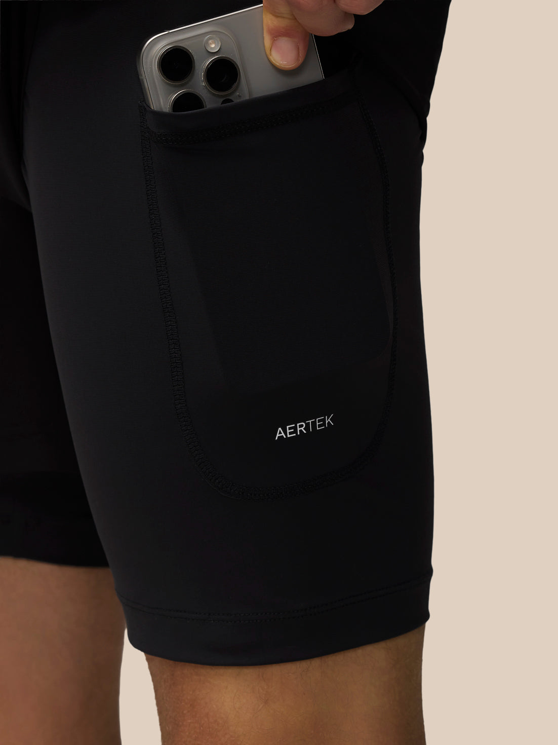 Person placing a smartphone into the outer side pocket of black Flow 2-in-1 shorts