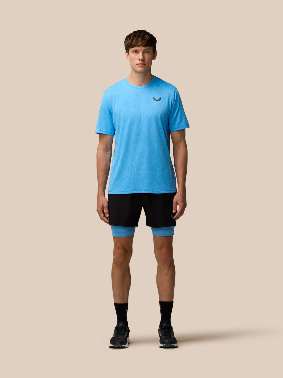 Full body shot of a male model wearing Flow 2-in-1 Shorts black with blue undershorts and a light blue patterned T shirt.