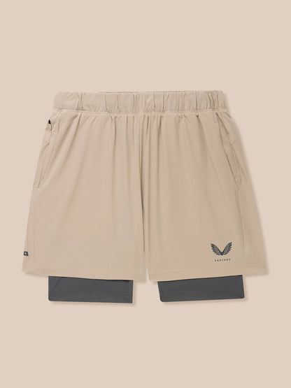 Beige Flow 2-in-1 shorts with blue undershorts peeking from the hem and Castore logo on the leg