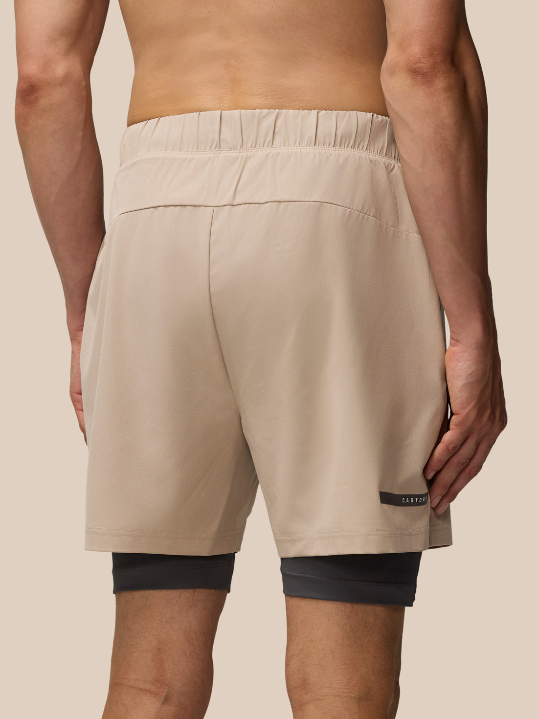 Back view of a male model wearing Flow 2-in-1 Beige shorts with dark undershorts visible beneath