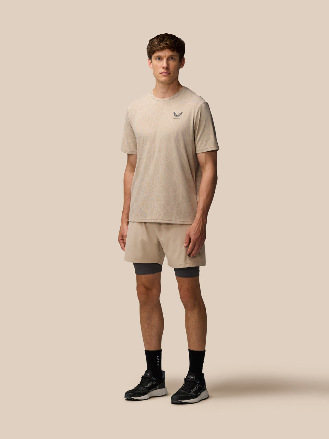 Full body view of a male model wearing Flow 2-in-1 Beige shorts with a matching beige top