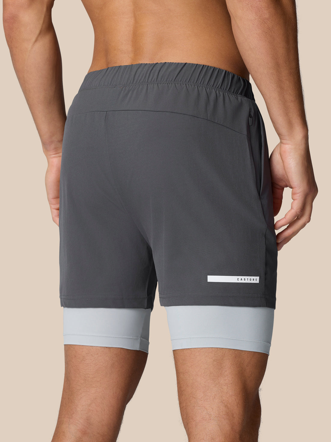 Back view of dark grey Flow Training 2-in-1 shorts with inner layer peeking at the hem and Castore logo