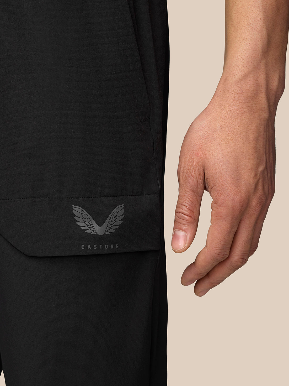Close up of pocket area on black cargo trousers with bonded flap and Castore emblem.