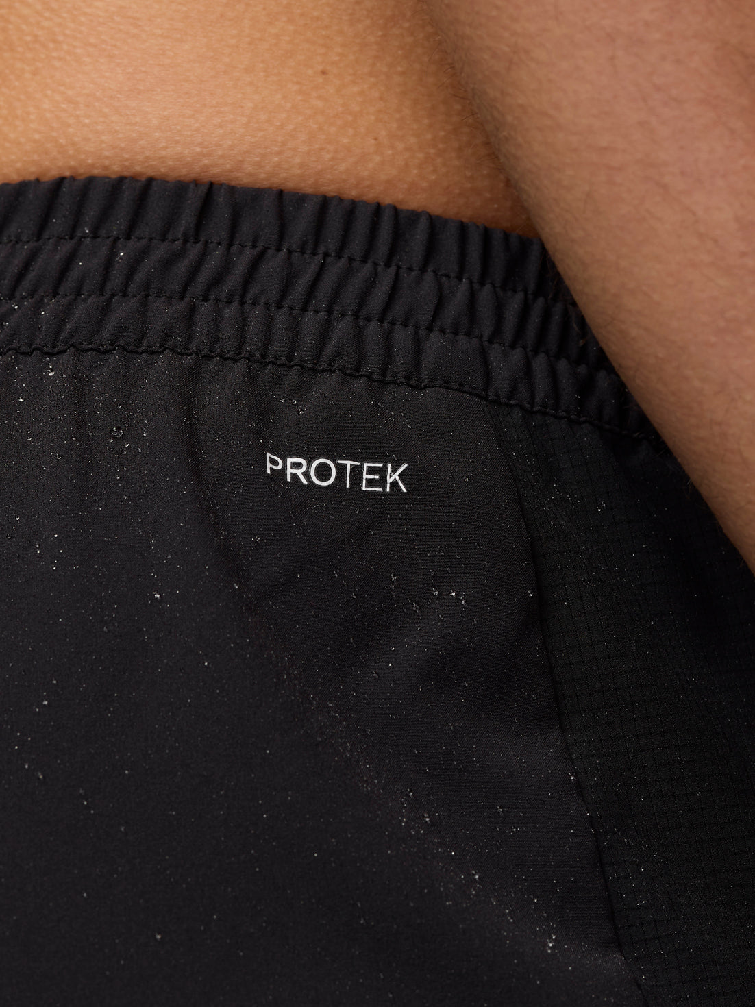 Close-up of the black Apex Shorts fabric near the waistband with Protek branding.
