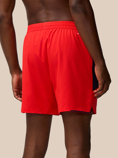 Close up of red Apex Training Shorts hem with navy side panel and white Castore logo
