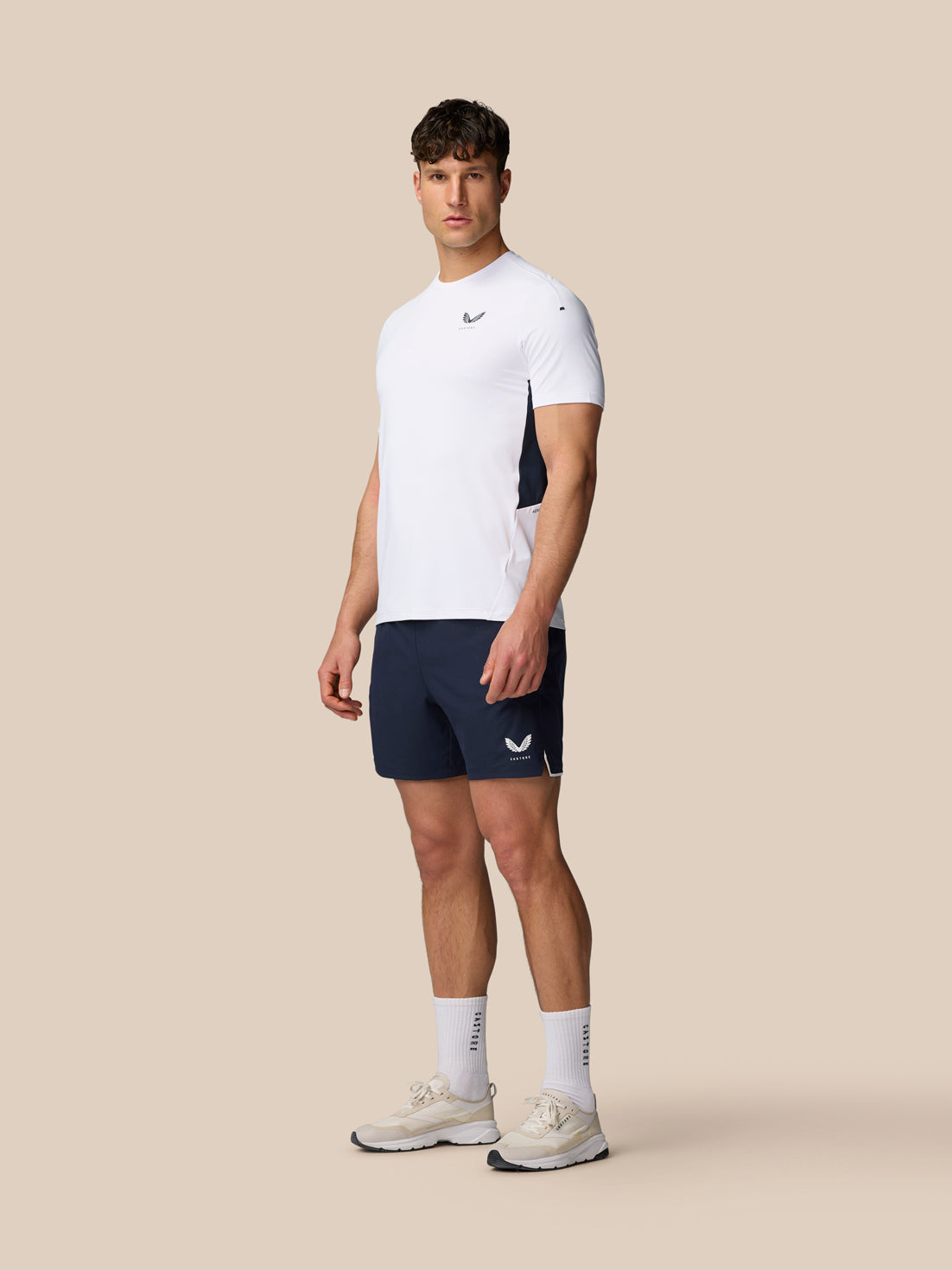 Full-body front view of a man in a white Apex Training T-Shirt and navy shorts with Castore logos