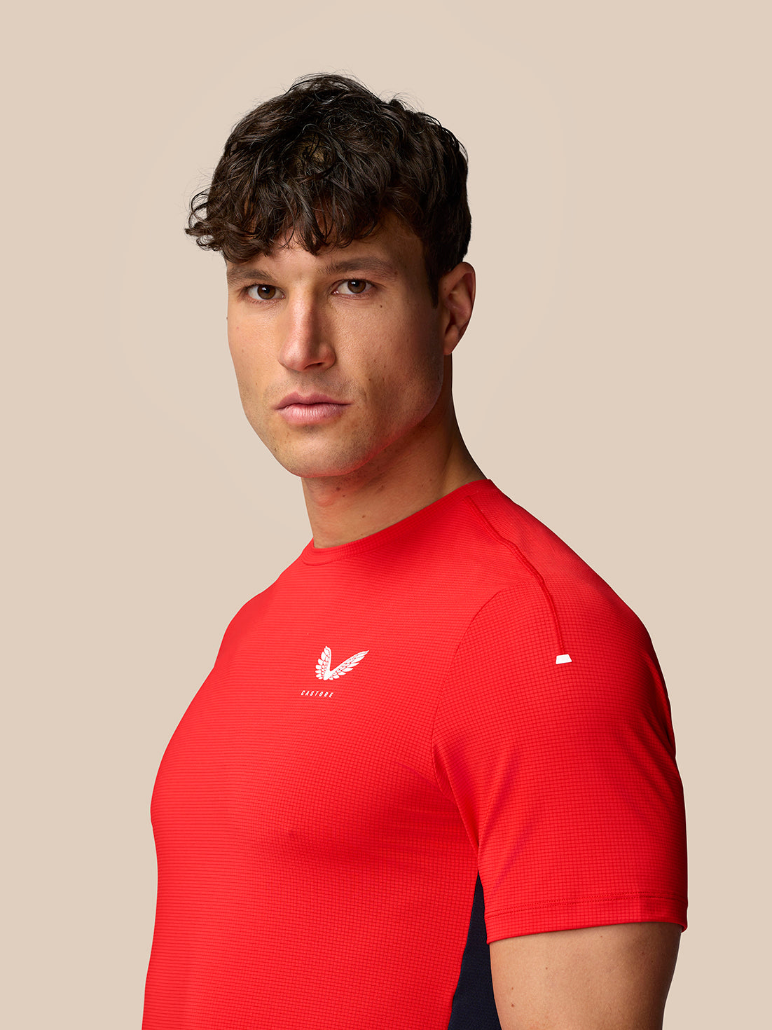 Side profile of male model in red Apex Training T Shirt showing chest logo and navy shorts