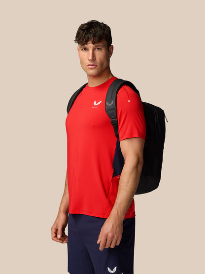 Male model wearing red Apex Training T-Shirt with navy shorts and backpack, side profile.