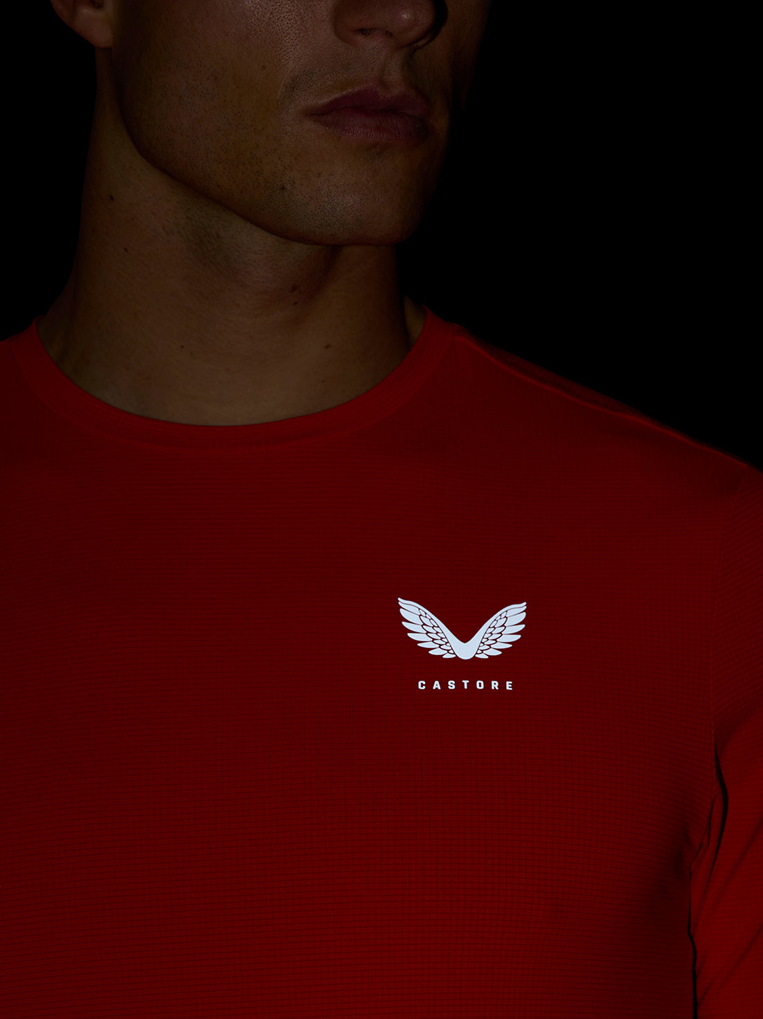 Close-up of a male model wearing a red Apex Training T-Shirt with a white Castore wing logo on the chest.