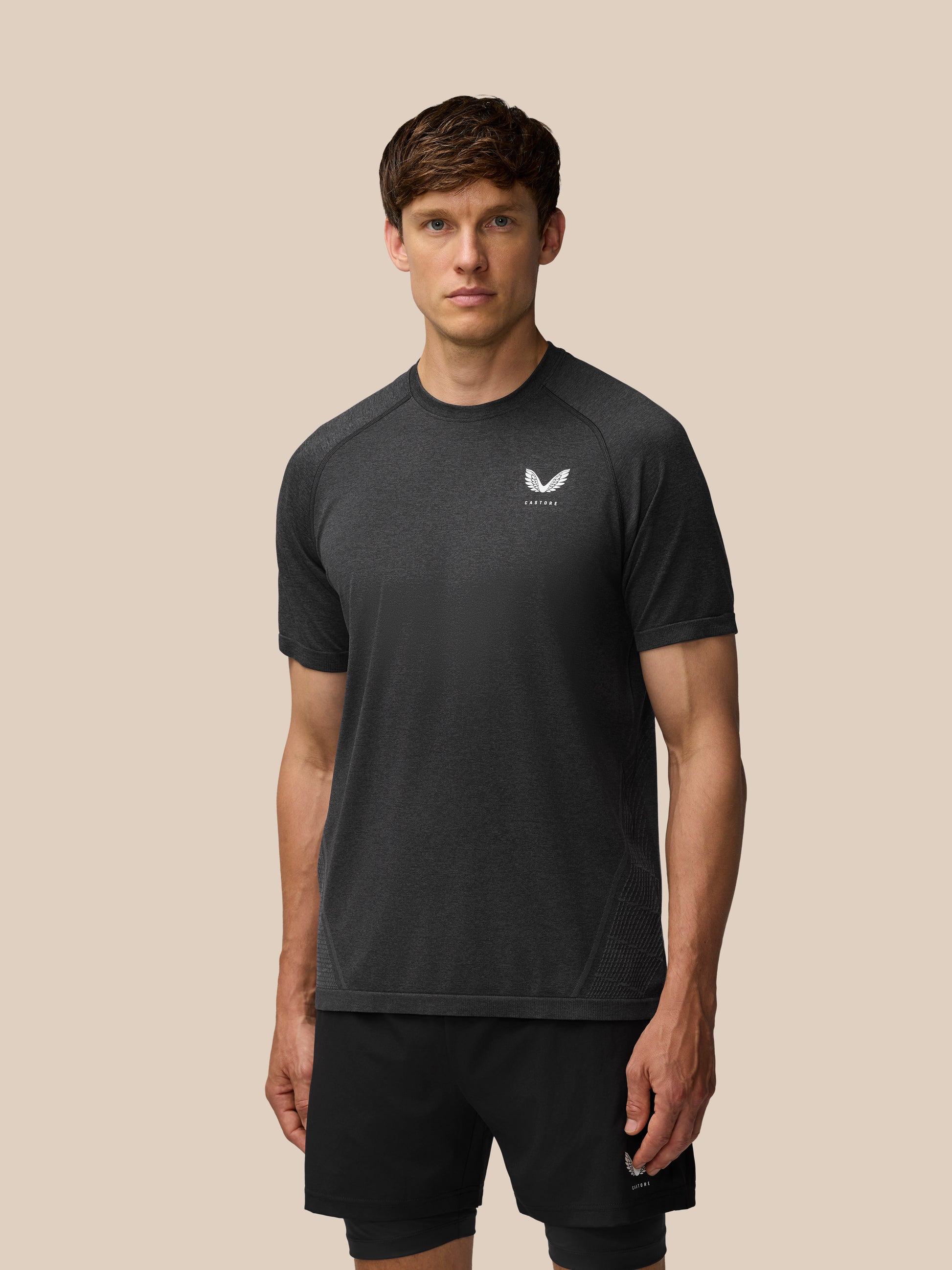 Man wearing black Flow Training T Shirt with white logo on the chest against a beige backdrop