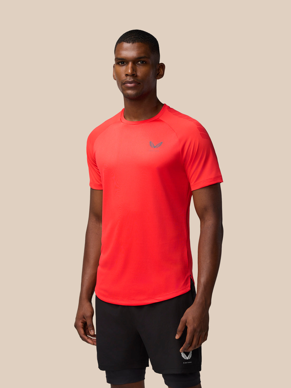 Athletic model wearing Flow Training Muscle Grip T-Shirt in Poppy red with black shorts against a beige backdrop