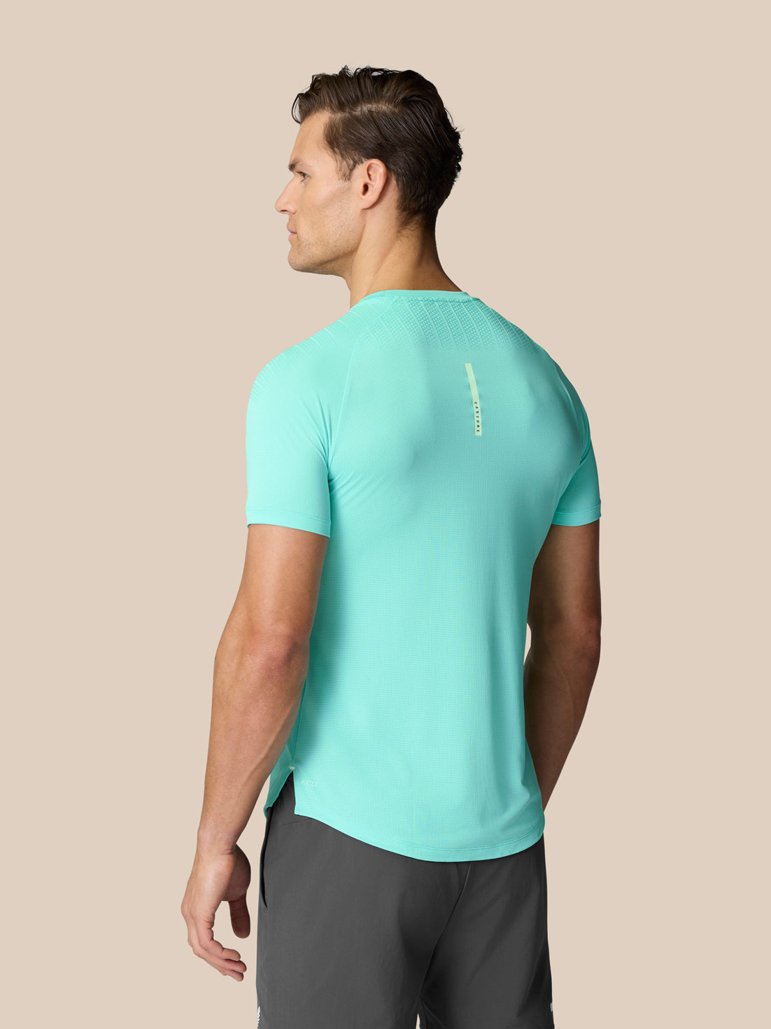 Back view of Flow Training Muscle Grip T-Shirt in Light Aqua on a male model showing back logo and curved hem.