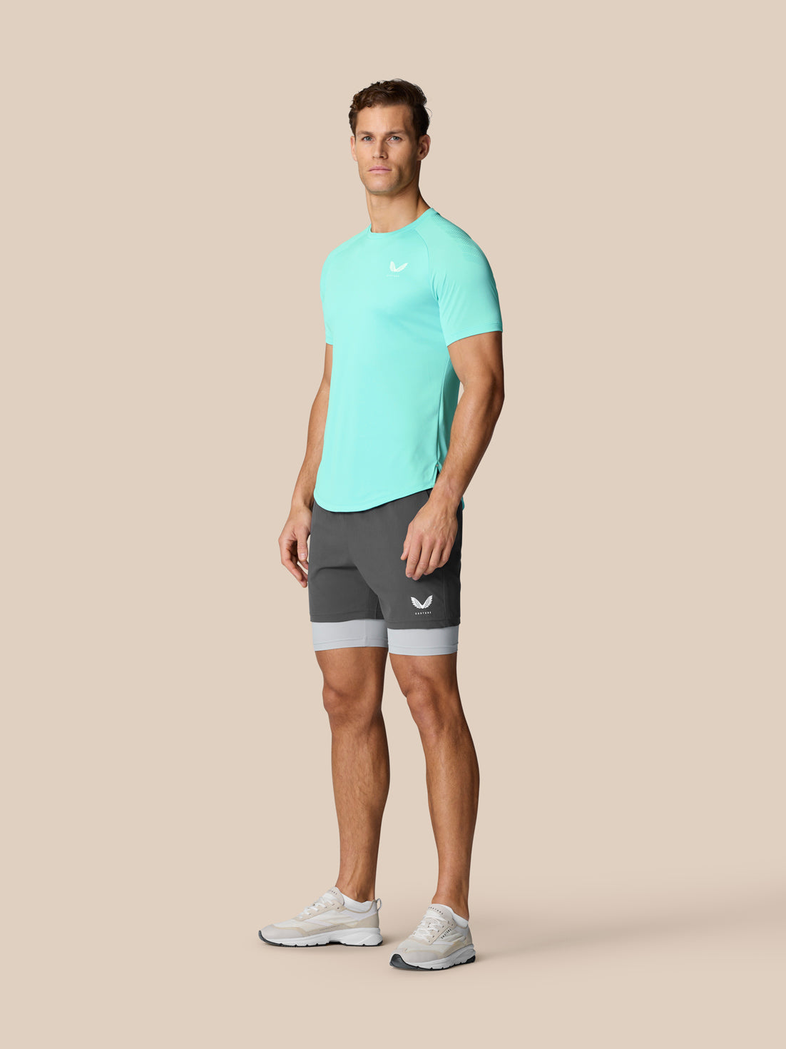 Male model wearing light aqua Flow Training Muscle Grip T-Shirt with logo on chest and grey shorts.