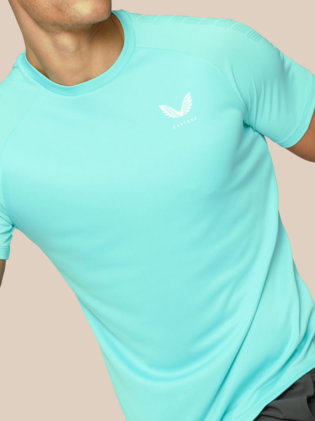 Model wearing light aqua Flow Training Muscle Grip T Shirt close up of chest with white winged logo and textured fabric
