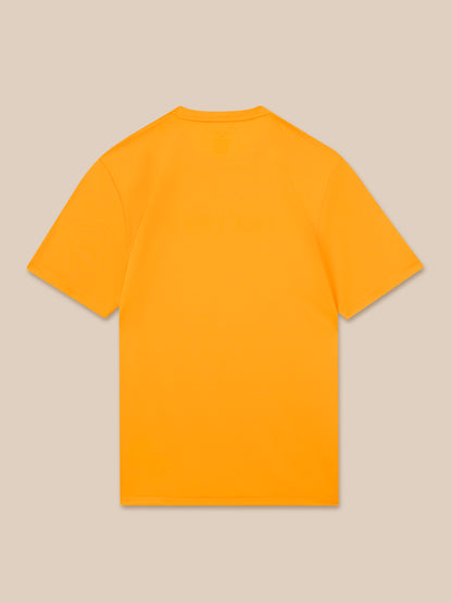 Back view of a bright mango T-shirt against a beige background.
