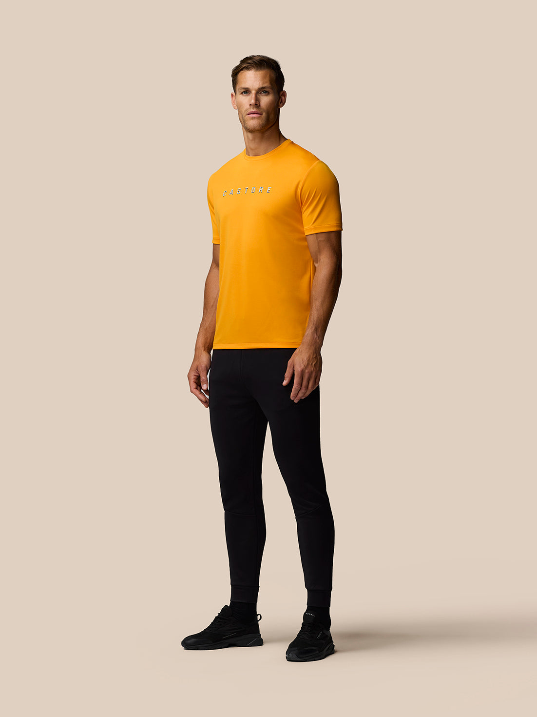 Male model wearing bright Mango graphic training T-shirt with Castore logo, black joggers and trainers.