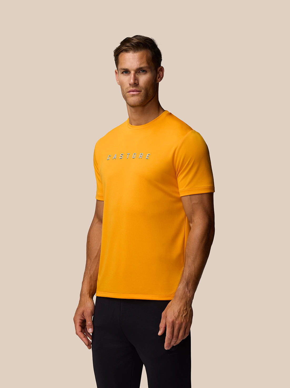 Male model in mango orange crew neck graphic training T shirt with Castore logo on chest