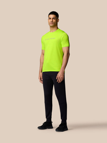 Male model wearing neon lime Castore Graphic Training T-Shirt with split hem and black joggers against a beige backdrop